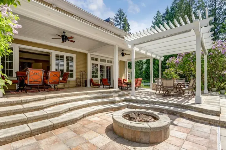 Pergola attached to a house above a paver patio with a fire pit