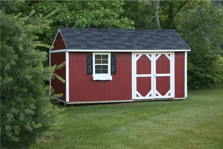 Long red board and batten storage shed with white trim, black shutters, double doors, and a dark shingled roof