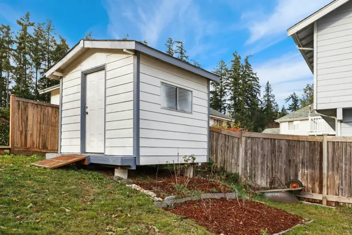 Shed-roof storage building raised on concrete pier blocks with a timber ramp running up to the door