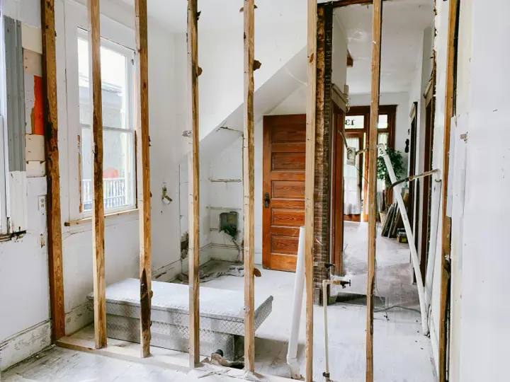 Interior of an occupied house stripped back to bare studs where partition walls have been opened up, with the original trim and doors still in place beyond