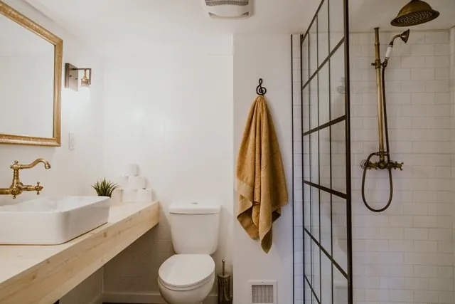 Renovated Red Deer bathroom with a floating wood vanity, vessel sink, gold fixtures, and a black-framed glass shower
